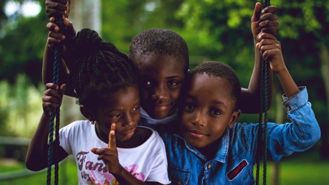 Three children sit on a swing.