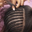 A mother doing cornrow styles in her daughter's hair