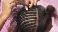 A mother doing cornrow styles in her daughter's hair