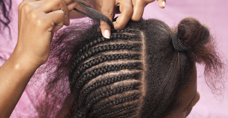 A mother doing cornrow styles in her daughter's hair