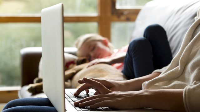 An adoption social worker uses her laptop while her daughter naps on the couch.