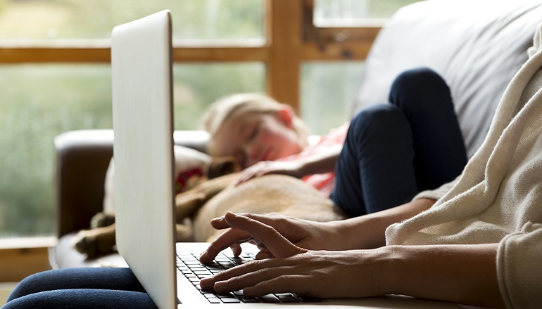 An adoption social worker uses her laptop while her daughter naps on the couch.