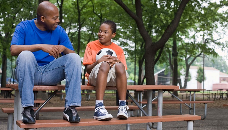 Parenting teens: a dad sits outside with his son at a picnic table