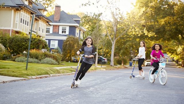 Three girls ride scooters and bikes during a play date.