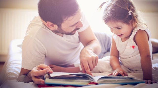 A dad works on building reading skills with his daughter by reading a book together.