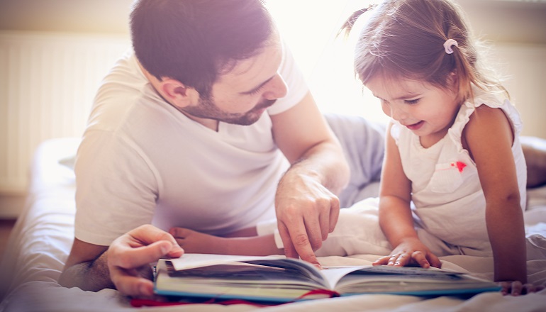 A dad works on building reading skills with his daughter by reading a book together.