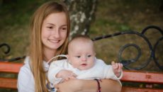 A teen sister holds her new sibling baby brother in the park