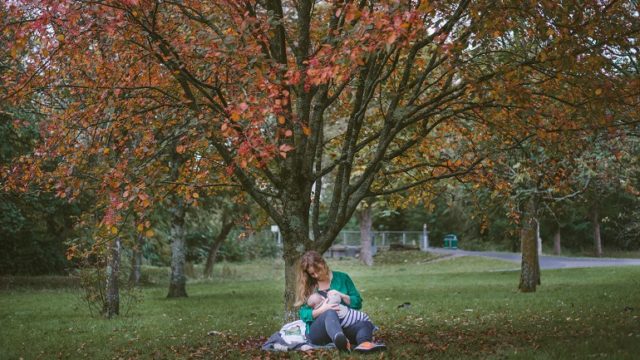 A woman sits in a park, breastfeeding an adopted baby