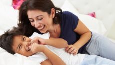 Mother And Son Lying In Bed Together Looking At Each Other Laughing. One example of connecting with kids.