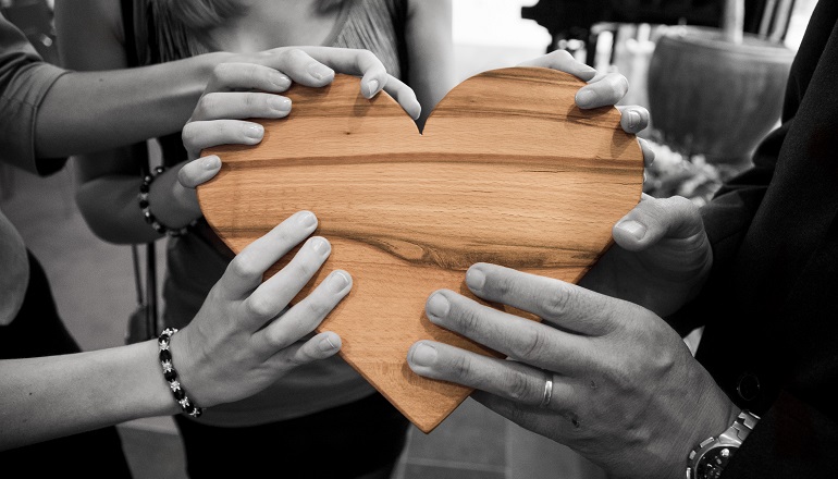 A group of people stand together, holding a wooden heart after adoption reunions