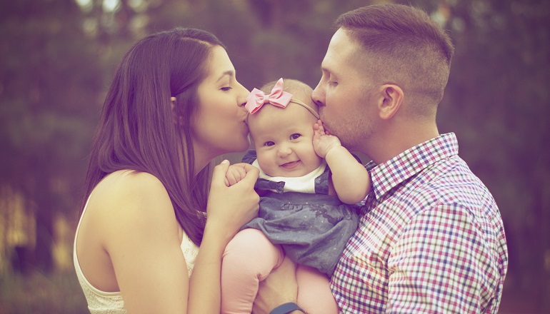 Two parents kiss their infant on the cheeks after preparing for a baby to adopt for so long.