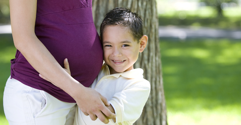 A young boy, adopted from Guatemala, hugging a woman's pregnant belly