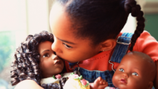 An African-American girls plays with two dolls that reflect her race