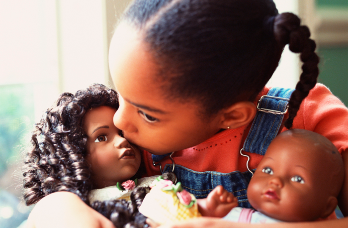 An African-American girls plays with two dolls that reflect her race