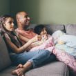A dad watches a adoption movies with his two children on the couch
