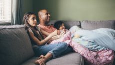 A dad watches a adoption movies with his two children on the couch