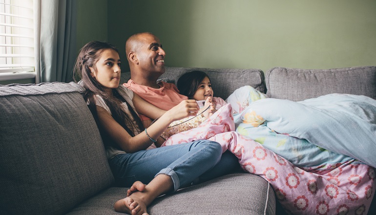 A dad watches a adoption movies with his two children on the couch