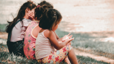 three friends sitting on grass, talking about adoption