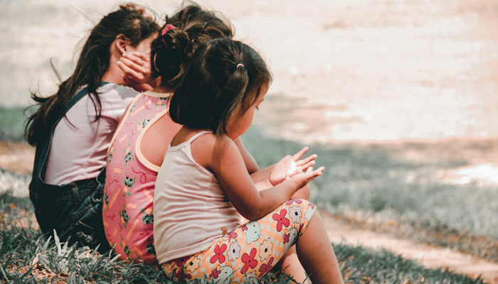 three friends sitting on grass, talking about adoption